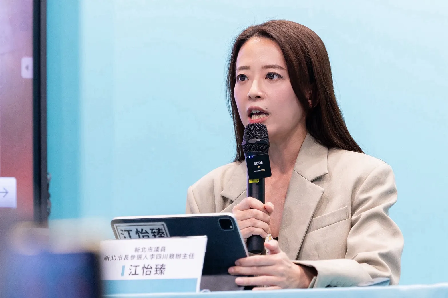 江怡臻手持麥克風發言，針對蘇巧純董事身分及親屬關係揭露提出質疑。（圖/李四川競辦提供)