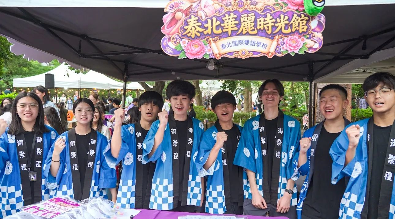 泰北學生穿上藍色祭典服裝，在活動攤位前合影，展現服務熱情。（圖/泰北國際雙語學校提供）