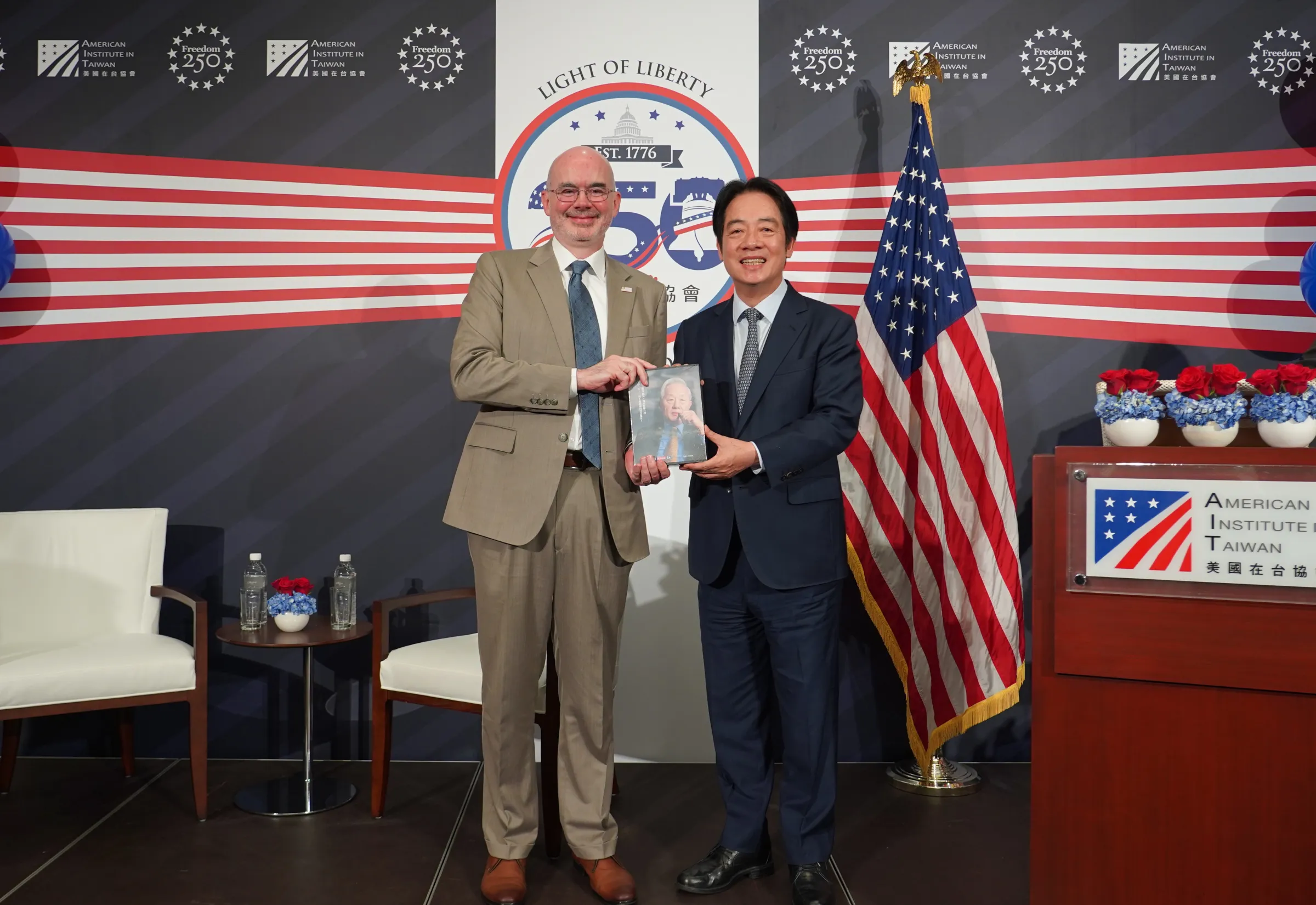 20260527-總統賴清德(右)27日晚間出席AIT慶祝酒會,稱要請AIT台北辦事處長谷立言(左)轉交《張忠謀自傳》全冊給美國總統川普。(美國在台協會提供)