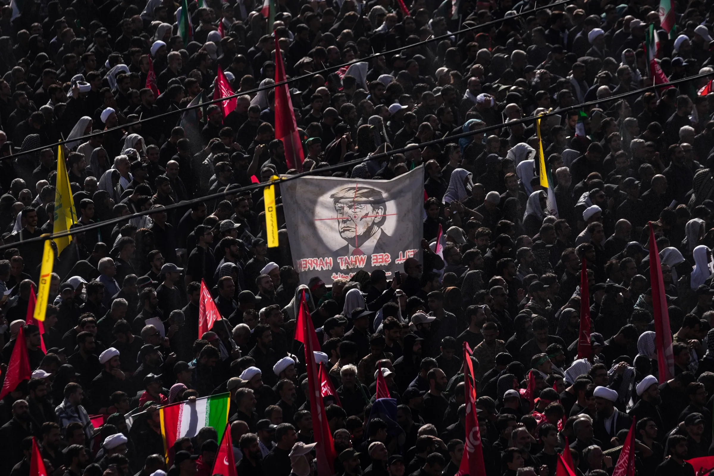 2026年7月5日、イランの首都テヘランのイマーム・ホメイニ・モスクで、故最高指導者・ハメネイ氏と家族の葬儀に参列する人々。狙撃銃のスコープで狙われるトランプ氏が描かれた旗を掲げる参加者の姿も見られた。(AP通信)